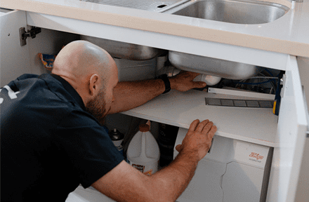 ZC plumber working on the drain and pipework under a kitchen sink
