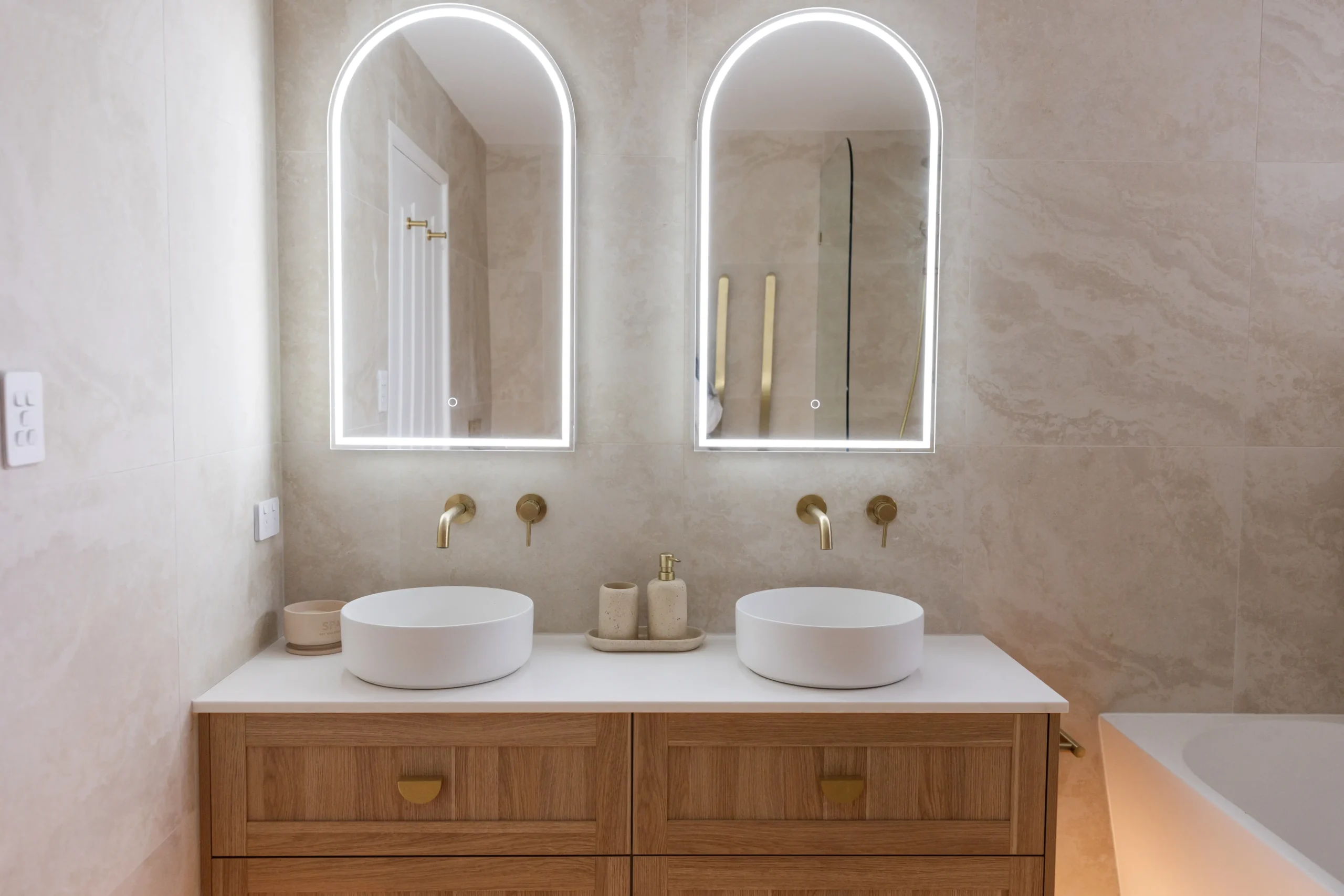 Completed bathroom renovation with backlit arched mirrors, twin basins and a timber vanity by ZC Plumbing, Central Coast