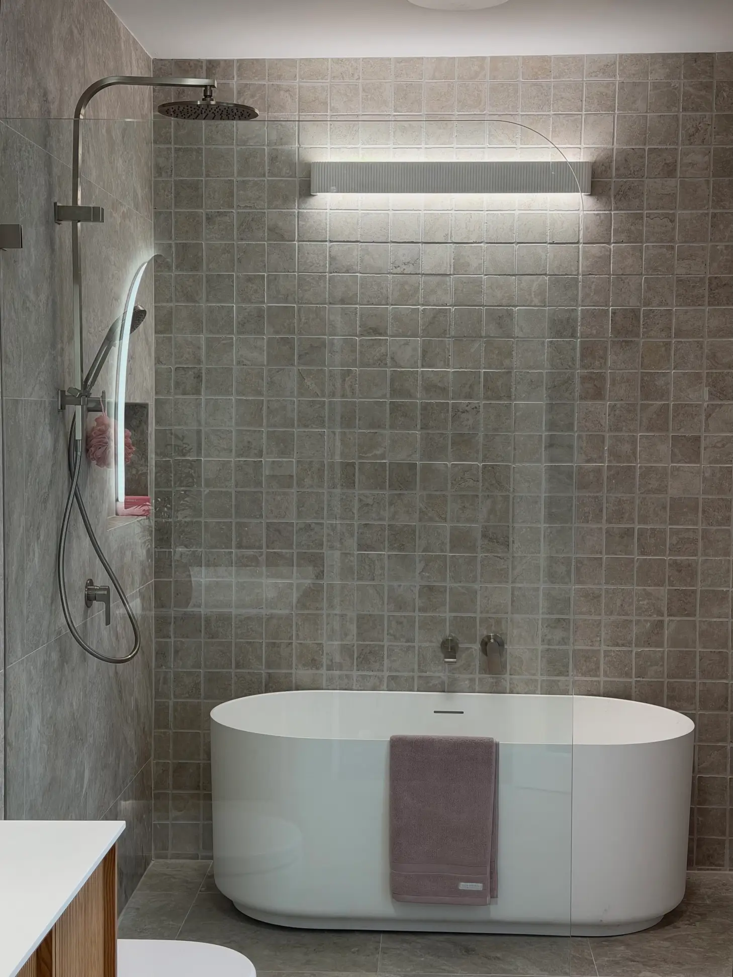 Bath beneath a rain shower with grey tiles in a Central Coast bathroom renovation