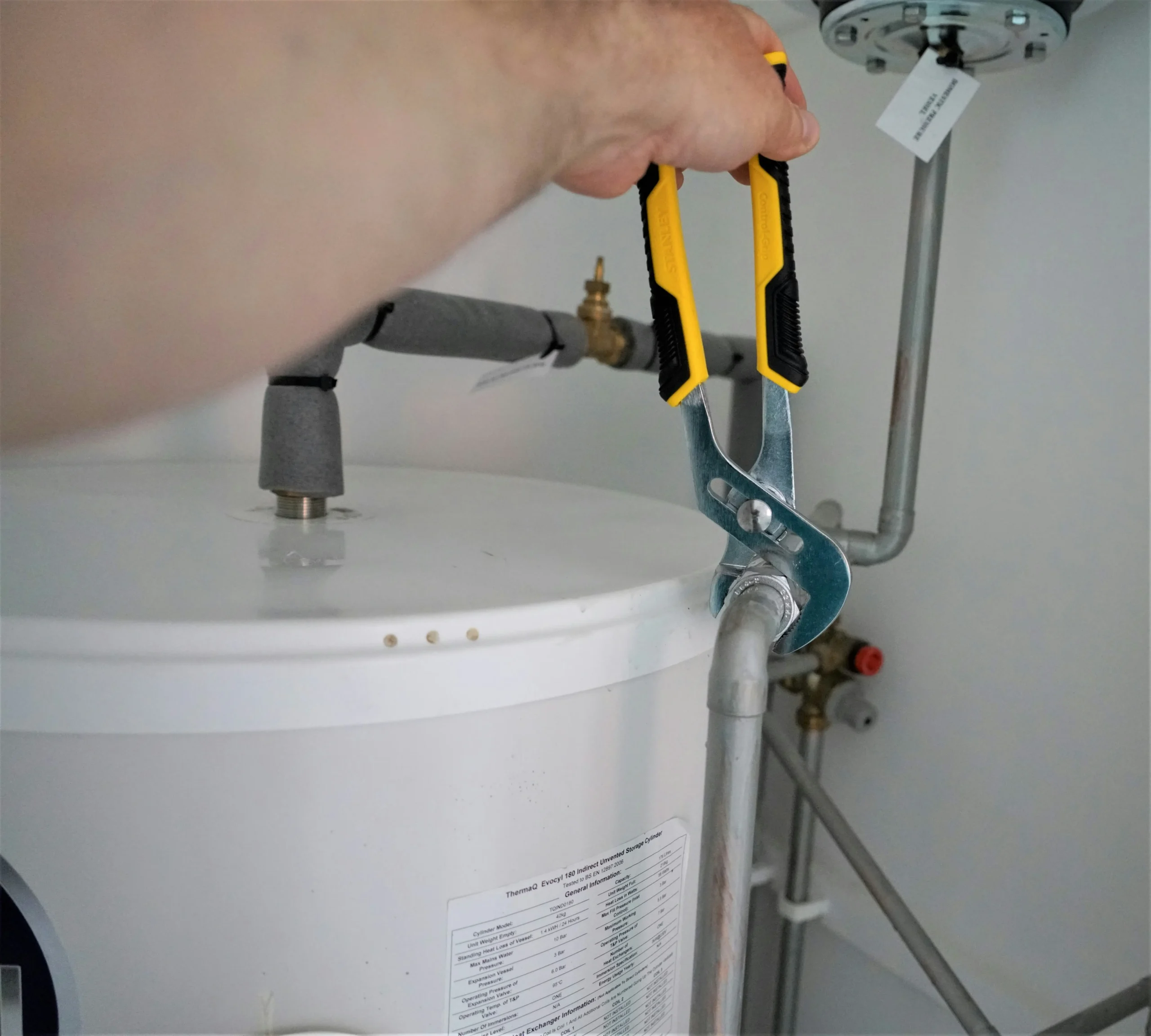Plumber servicing the fittings on top of a hot water storage tank