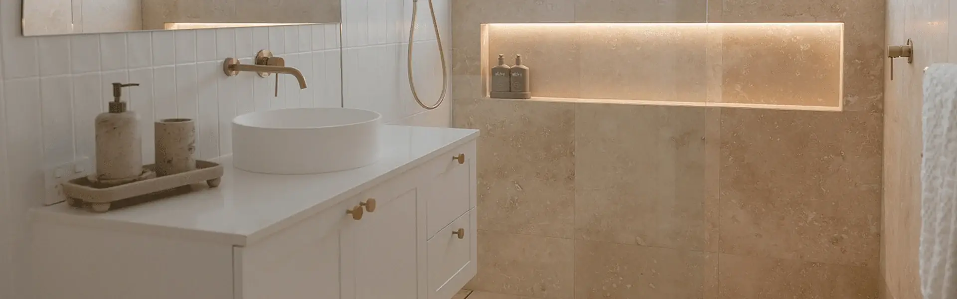 Renovated bathroom with a white vanity, brass tapware, hand shower and LED-lit travertine niche by ZC Plumbing & Bathroom Solutions, Central Coast